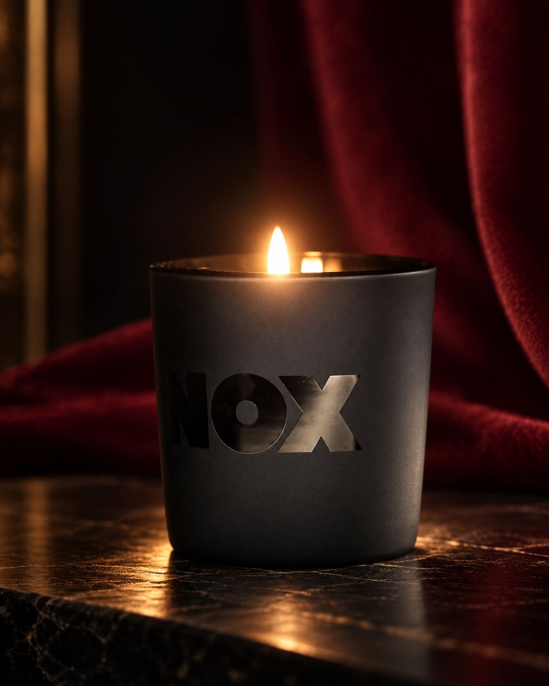 Το NOX Signature Candle αναμμένο, σε ματ μαύρο γυαλί με γυαλιστερό λογότυπο NOX